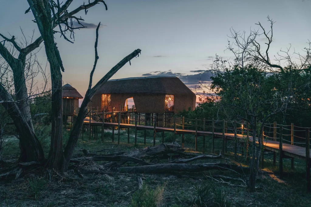 An image of a thatch building with an elevated boardwalk at sunset