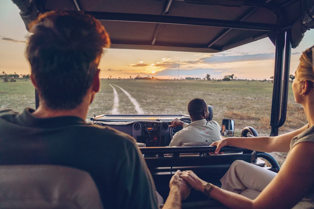 Guests on a sunset game drive in the Okavango Delta, silhouetted against golden skies with open plains in the background.