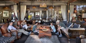 A family relaxing and playing board games in the luxury common area of Atzaró Okavango Camp, featuring elegant African decor and a safe, spacious lounge.