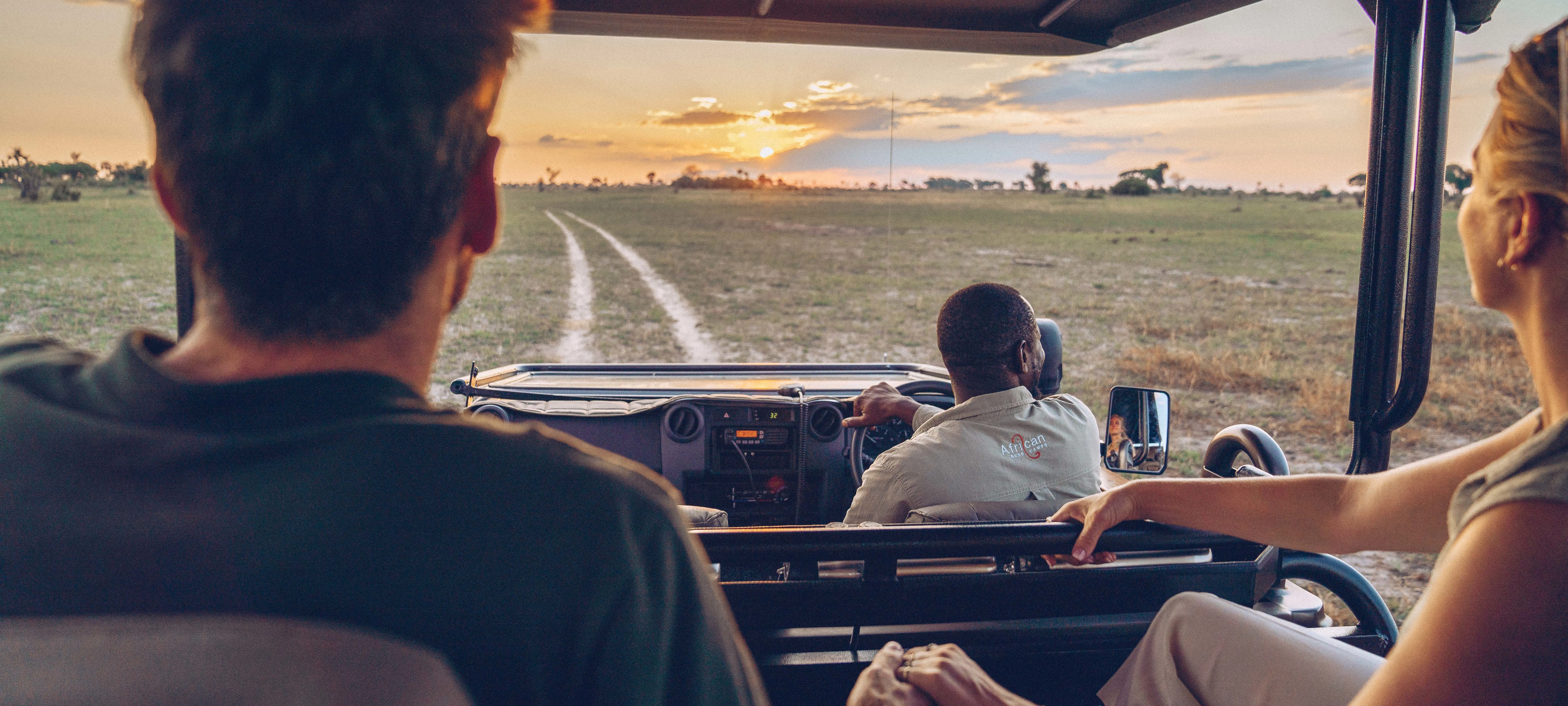 Couple in safari vehicle with guide during game drive at Atzaró Okavango Camp, Botswana.