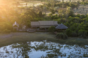 Aerial drone view of Atzaró Okavango Camp main lodge area nestled among trees and wetlands in the Okavango Delta, Botswana, at sunrise.