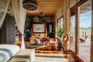 Interior of a luxury safari suite at Atzaró Okavango Camp, Botswana, featuring elegant wooden floors, a private lounge area, and floor-to-ceiling windows overlooking the Delta.