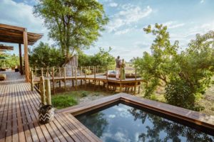 A luxury safari suite's private wooden deck featuring a plunge pool and a couple standing on a lookout platform overlooking the Okavango Delta, Botswana.