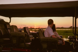 Una pareja en un vehículo de safari disfruta del atardecer durante una salida de observación de fauna organizada por Atzaró Okavango Camp.